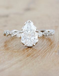 a pear shaped diamond engagement ring on top of a wooden table with white gold band