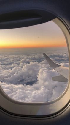 an airplane window looking out at the clouds and sunset over the ocean in the distance