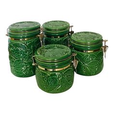 four green glass jars with gold trimmings and leaf designs on the lids are lined up