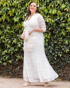 a woman in a white dress standing next to some bushes