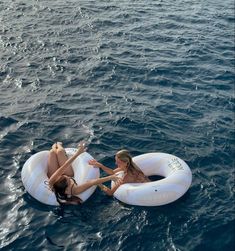 two girls are floating on inflatable rafts in the middle of the ocean