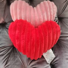 a red heart shaped pillow sitting on top of a gray couch with a price tag