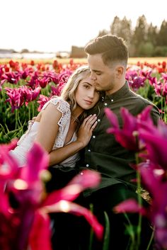 a man and woman sitting in the middle of a field full of pink tulips