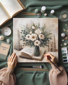 a woman is painting flowers in a vase on an open book, surrounded by other items