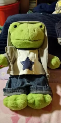 a green stuffed animal sitting on top of a bed next to a blue and white pillow