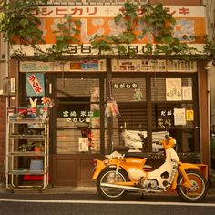 an orange and white motorcycle parked in front of a store with plants growing on the windows