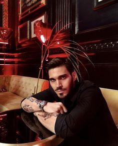 a man sitting at a table with tattoos on his arms and arm, in a restaurant