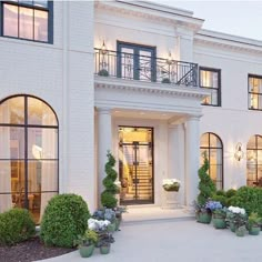 a large white house with lots of windows and plants in the front yard at dusk