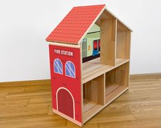 a wooden toy fire station with a red roof and two shelves on the floor next to it