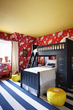 a child's bedroom with red and white wallpaper, black bunk bed, yellow stools, and striped rug