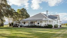 a large white house sitting in the middle of a lush green field with lots of trees