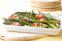 asparagus and tomatoes in a white dish on a yellow tablecloth with plates