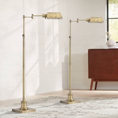 two brass floor lamps in a living room with white walls and rug on the floor