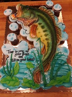 a birthday cake with a large fish on it and cupcakes in the background