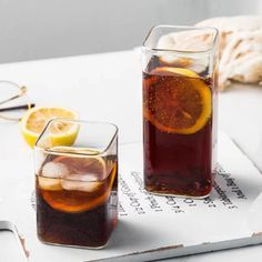 two glasses filled with liquid sitting on top of a table next to sliced lemons