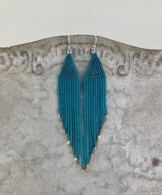 a pair of blue beaded earrings hanging from a hook on top of a stone wall