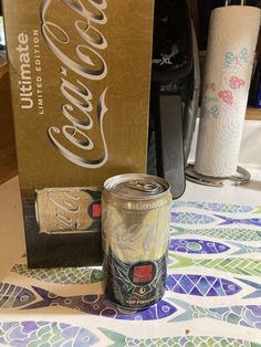 a can of coca - cola next to an unopened box on a table