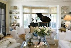 a living room filled with furniture and a grand piano in the window sill next to a coffee table