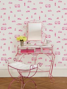 a pink vanity table with a mirror and flowers on it in front of a wallpapered background