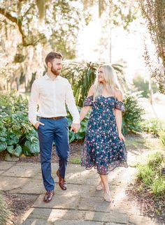 an engaged couple holding hands and walking through the park