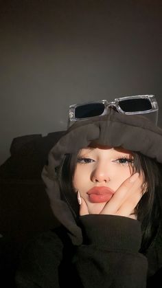 a woman with her hands on her face, wearing sunglasses and a black hoodie