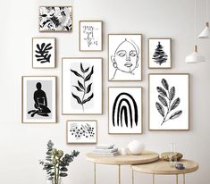 there are many framed pictures on the wall above a table with a vase and potted plant