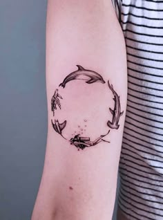 a black and white photo of a dolphin in a circle tattoo on the left arm