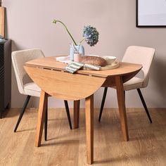 a wooden table with two chairs and a vase on top of it in front of a pink wall