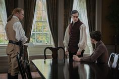 three people standing around a dining room table with chairs and one person holding a cane