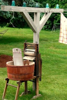 an old fashioned washing machine and bucket in the grass with clothes hanging out to dry