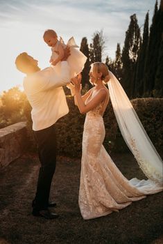 a man holding a baby in his arms while standing next to a woman wearing a wedding dress