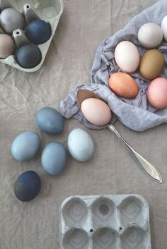 an assortment of eggs in trays on a table with utensils next to them