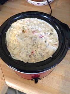 a crock pot filled with food sitting on top of a wooden table next to a bowl