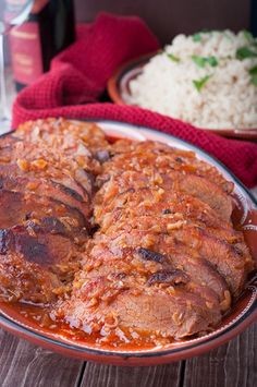 some meat and rice on a plate with red cloths next to the bowl full of rice