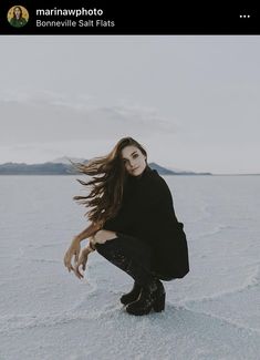 a woman kneeling down in the snow with her long hair flying through the air and looking at the camera