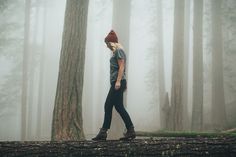 a woman walking in the woods on a foggy day with her foot up and wearing a beanie