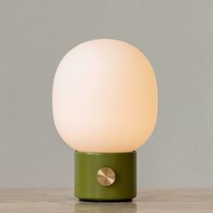 a green table lamp sitting on top of a wooden table next to a gray wall