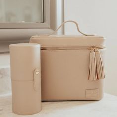 Pictured is a rectangle nude bag that includes an all around zipper with tassel pulls and a top handle. This picture includes a nude cylinder brush holder and is all pictured on a off white background. Circle E Candles, Brush Holders, Athleisure Shoes, Beauty Blenders, A Place For Everything, Bag Obsession, Travel Games, Travel Set, Travel Collection