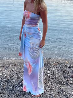 a woman is standing on the beach wearing a blue and pink dress with seashells all over it