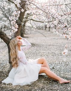 a woman sitting in front of a tree wearing a white dress