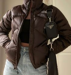 a woman wearing a brown puffer jacket and holding a black purse in her right hand