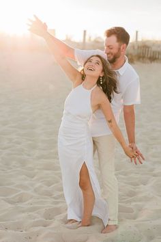 a man and woman standing on top of a sandy beach holding each other's hands