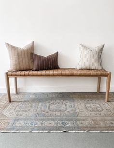 a wooden bench sitting on top of a rug next to two pillows and a rug