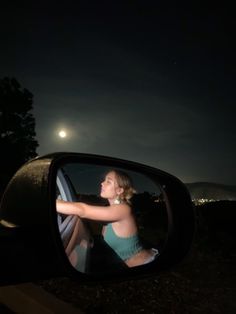 a woman taking a selfie in the side view mirror of a car at night