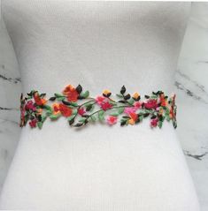 a white dress with colorful flowers on it's waist and an embroidered belt around the waist