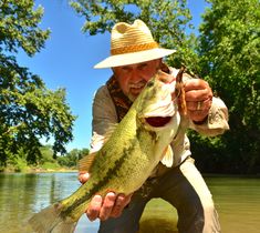 a man in a hat holding a large fish while standing in the water on a sunny day