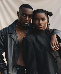 two people standing next to each other in front of a white wall and wearing black clothing