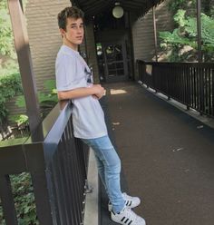 a young man leaning on a railing in front of a building with trees and bushes