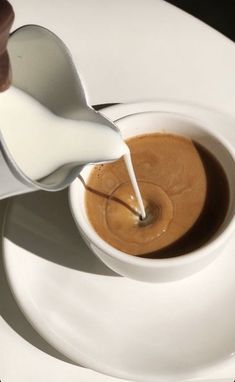 a person pouring milk into a cup on top of a white plate with a spoon