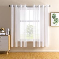 a window with white sheer curtains in front of a wooden dresser and side table on hard wood flooring